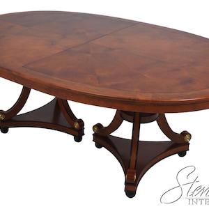 May include: A large oval wooden dining table with a dark wood finish and a leaf extension. The table has a pedestal base with three legs and a decorative scroll design. The table is on wheels and has a brass accent.