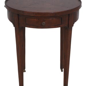 May include: A dark brown, round side table with a single drawer and four slender legs. The table has a raised edge and small brass casters on the feet. The drawer features a decorative knob.
