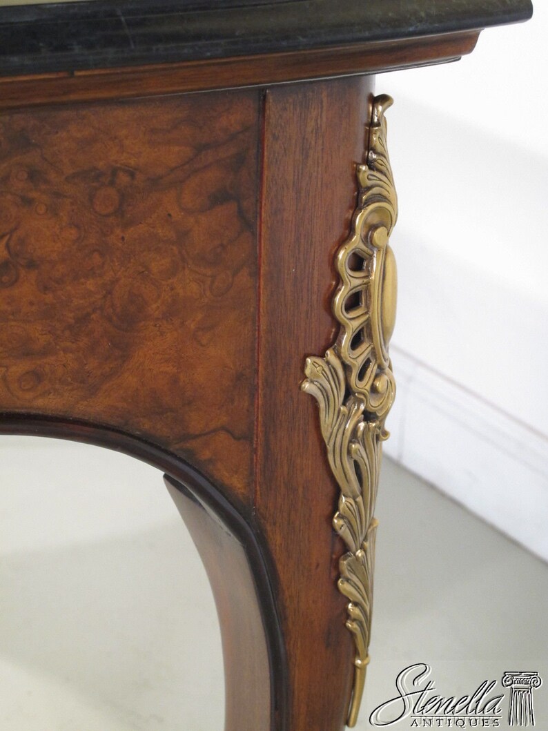May include: A close-up of a wooden table leg with a decorative brass accent. The table leg is curved and has a dark brown finish. The brass accent is ornate and features a floral design.