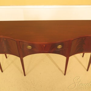 Pu&ograve; includere: Un credenza in legno di mogano con un fronte curvo e tre cassetti. La credenza ha una finitura marrone rossiccio scuro e ferramenta in ottone.