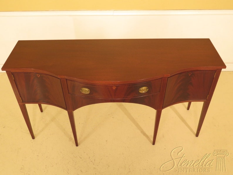 Pu&ograve; includere: Un credenza in legno di mogano con un fronte curvo e tre cassetti. La credenza ha una finitura marrone rossiccio scuro e ferramenta in ottone.