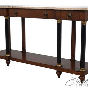 May include: A rectangular wooden console table featuring a light beige marble top, four drawers with circular brass pulls, and four black cylindrical columns with brass accents. The base includes a lower shelf and four turned wooden feet.