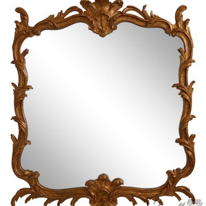 May include: A gold-toned ornate mirror with a decorative, scrolled frame. The mirror has a slightly arched top and a beveled edge.