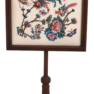 May include: A wooden fire screen with a floral embroidered panel featuring a bird, flowers, and butterflies. The screen has a turned wooden post and a tripod base.