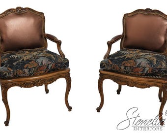 May include: Two ornate wooden armchairs with carved details. The chairs have a brown leather back and a floral patterned fabric seat.