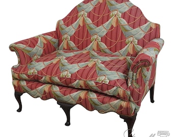 May include: A red and green patterned fabric loveseat with a curved back and wooden legs. The fabric features a repeating pattern of blue and green ribbons with gold accents.