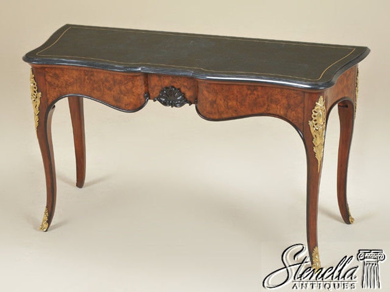 May include: A French-style console table with a black leather top and intricate wood marquetry. The table has ornate gold accents and curved legs.