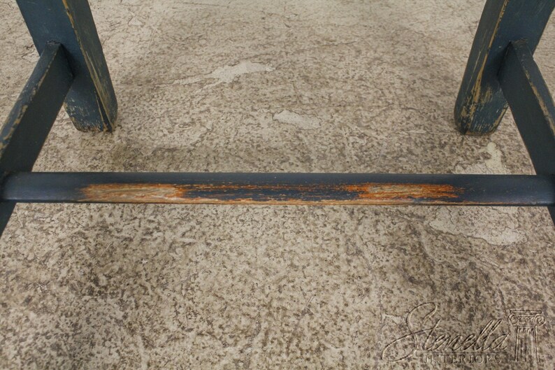 Op de afbeelding: Close-up van de onderkant van een houten stoel met een donkerblauwe verfbehandeling. De stoel heeft een versleten, verweerde uitstraling met wat hout dat door de verf heen zichtbaar is.