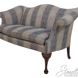 May include: A two-seater sofa with a patterned fabric in shades of blue, gray, and pink. The sofa has curved arms and a high back. The wooden legs are dark brown.