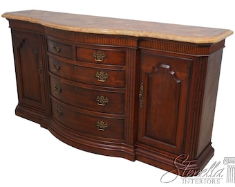 May include: A curved mahogany sideboard with five drawers and two doors. The top is made of marble with a decorative inlay. The sideboard has brass hardware and a dark wood finish.