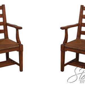 May include: Two wooden armchairs with a ladder back design and woven seats. The chairs are a warm brown color and have curved armrests. The chairs are set against a white background.