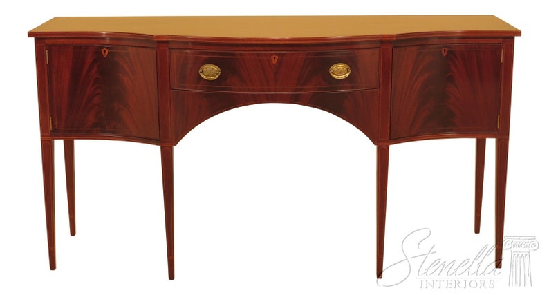 Pu&ograve; includere: Un credenza in legno di mogano con due ante e un cassetto. La credenza ha un fronte curvo e poggia su quattro gambe sottili.