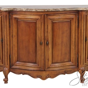 May include: A wooden sideboard featuring a curved front with four cabinet doors, a marble top with brown and beige veining, and carved cabriole legs. The piece has a medium brown finish and includes the text Stemella Interiors in the bottom right.