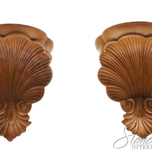May include: A pair of brown wall brackets featuring a carved shell design with fluted details and scroll accents at the base. The wooden-toned pieces have a symmetrical shape with a flat top surface and a decorative, textured front profile.