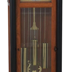 May include: A tall, wooden grandfather clock with a light-colored face and a pendulum visible through a glass door. The clock has a dark finish with black accents and decorative elements.