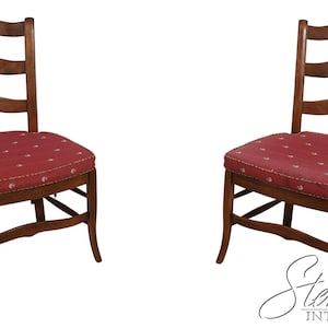 May include: Two wooden chairs with ladder backs and red cushions. The cushions have a white dotted pattern. The chairs have curved legs and are made of a dark wood. The chairs are set against a white background.