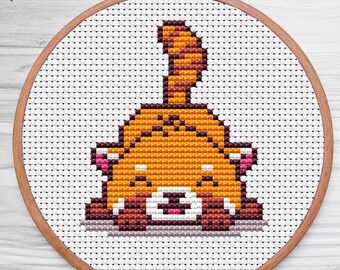 May include: A cross-stitch embroidery hoop with a cute cartoon red panda design. The panda is brown and orange with a white face and pink cheeks. The panda is sitting on its haunches with its tail curled up behind it.
