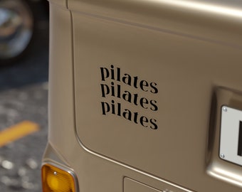 May include: A beige van with a black sticker that says "pilates pilates pilates" on the back. The van has a number plate on the back.