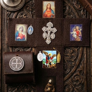 Puede incluir: Un expositor de fieltro marrón oscuro en forma de cruz con imágenes religiosas de Jesús, María, José, San Miguel y San Francisco. Incluye un crucifijo de plata, varias medallas de metal, un imperdible y una bolsa de cuero con una medalla.