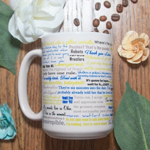 May include: White ceramic mug with a blue and yellow design featuring a variety of text, including quotes from popular TV shows and movies. The text includes phrases like "Deal with it", "Vomit free", "It's gunna be legen... wait for it... DARY", and "Thank you, next".