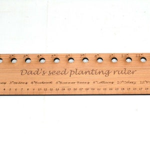 May include: A wooden ruler with holes for planting seeds. The ruler is marked in inches and has a label that says "Dad's seed planting ruler". The label also lists different types of vegetables and their recommended spacing: 2" Peas, 3" Onions, 4" Beetroot, 6" Runner Beans, 8" Lettuces, 10" Celery, 12" Potatoes.