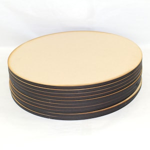 May include: A stack of round wooden craft blanks, each with a dark brown edge. The blanks are stacked on a white surface.