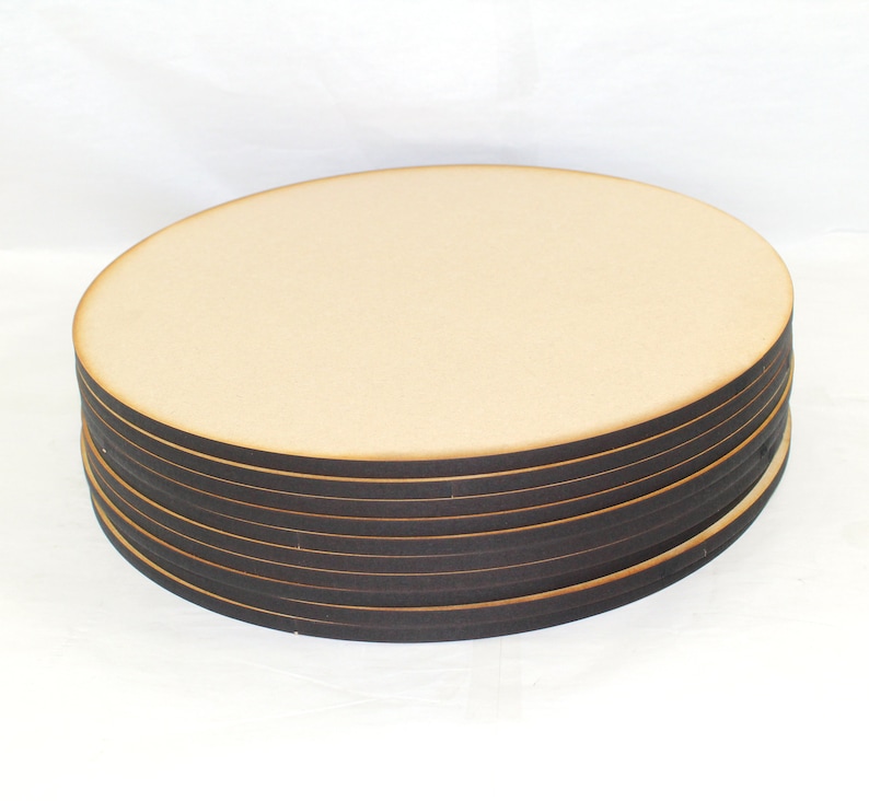 May include: A stack of round wooden craft blanks, each with a dark brown edge. The blanks are stacked on a white surface.
