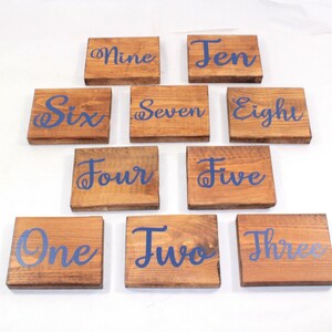 May include: Ten wooden signs with the numbers one through ten written in blue cursive on a brown wooden background.