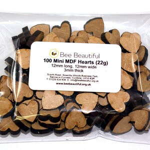 K&ouml;nnte beinhalten: Eine T&uuml;te mit 100 kleinen, braunen Holzh Herzen. Die Herzen sind 12 mm lang, 12 mm breit und 3 mm dick. Die T&uuml;te ist mit "Bee Beautiful 100 Mini MDF Hearts (22g)" beschriftet.