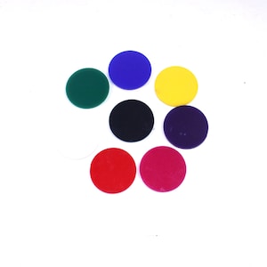 May include: Seven brightly coloured, circular objects are arranged on a white background. The objects are in shades of green, blue, yellow, black, purple, red, and pink. The objects appear to be made of a solid material.