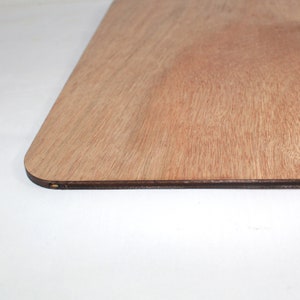 May include: A close-up of the edge of a rectangular wooden board with a rounded corner. The board is made of light brown wood with a natural grain pattern. The edge of the board is slightly darker than the rest of the surface.