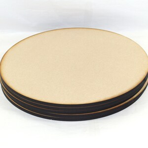 May include: A set of four round wooden coasters with black edges. The coasters are stacked on top of each other.