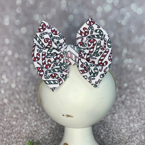 May include: A white headband with a bow made of white fabric with a red and green candy cane pattern.