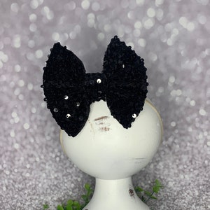 May include: A black velvet bow with silver glitter and rhinestones on a white stand.