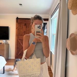 Puede incluir: Un bolso de mano peque&ntilde;o, rectangular y acolchado, confeccionado en tela de color crema con un estampado de pa&ntilde;uelo de cachemira en negro. El bolso cuenta con dos asas cortas de tela y una forma estructurada con costuras visibles en el exterior.