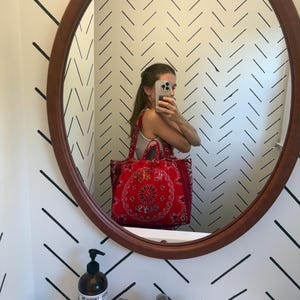 Puede incluir: Un bolso tote rojo con un estampado tradicional de bandana paisley en blanco y negro. El bolso tiene dos asas de tela e incluye un texto bordado en la parte frontal que dice "MARLOYS" con hilo claro sobre la tela roja.