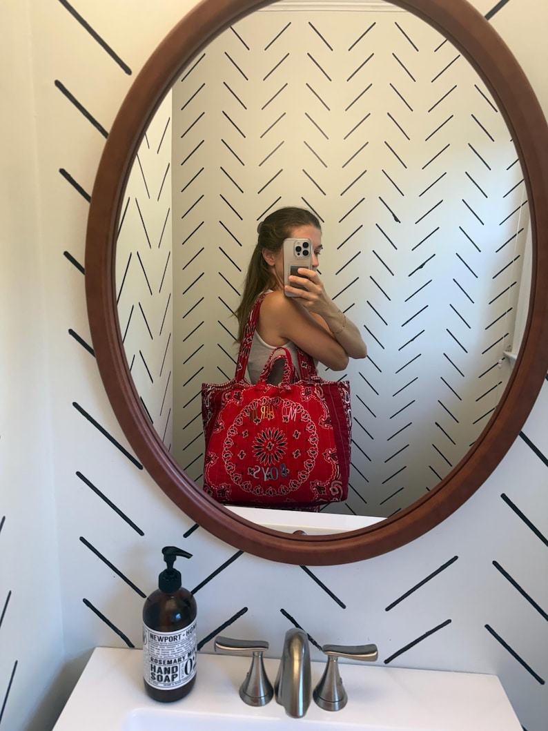 Puede incluir: Un bolso tote rojo con un estampado tradicional de bandana paisley en blanco y negro. El bolso tiene dos asas de tela e incluye un texto bordado en la parte frontal que dice "MARLOYS" con hilo claro sobre la tela roja.