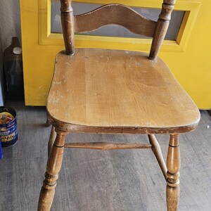 May include: A vintage wooden chair with a ladder back design. The chair features a light brown seat and backrest, with a darker brown finish on the ladder back. The legs are turned and tapered. The chair is set against a yellow door.