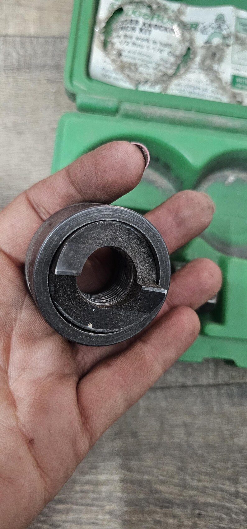 Puede incluir: Una herramienta de metal gris oscuro con un dise&ntilde;o circular y un interior roscado. La herramienta se sostiene en una mano, con una caja de pl&aacute;stico verde visible en el fondo. La herramienta parece ser parte de un conjunto m&aacute;s grande.