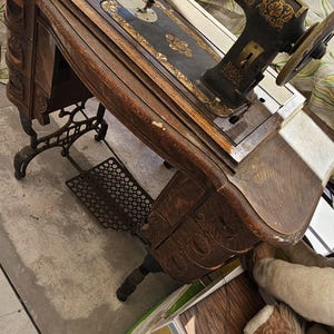 May include: Antique White Rotary sewing machine with a wooden cabinet. The machine is black with gold accents and the text "WHITE ROTARY U.S.A." is visible. The cabinet has ornate carvings and a foot pedal.