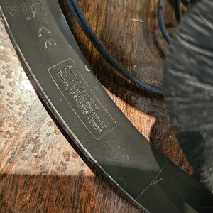Op de afbeelding: Zwarte hoofdtelefoon met een textuur op de hoofdband en een gedrukt label met de tekst Sony Corporation, 1-7-1 Konan Minato-ku, Tokyo, 108-0075 Japan, inclusief een CE-markering. Het apparaat bevat een zwarte kabel en gewatteerde oorkussens.