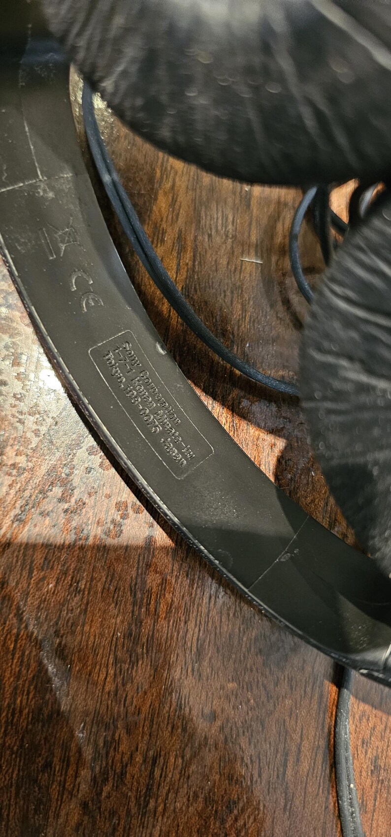 Op de afbeelding: Zwarte hoofdtelefoon met een textuur op de hoofdband en een gedrukt label met de tekst Sony Corporation, 1-7-1 Konan Minato-ku, Tokyo, 108-0075 Japan, inclusief een CE-markering. Het apparaat bevat een zwarte kabel en gewatteerde oorkussens.
