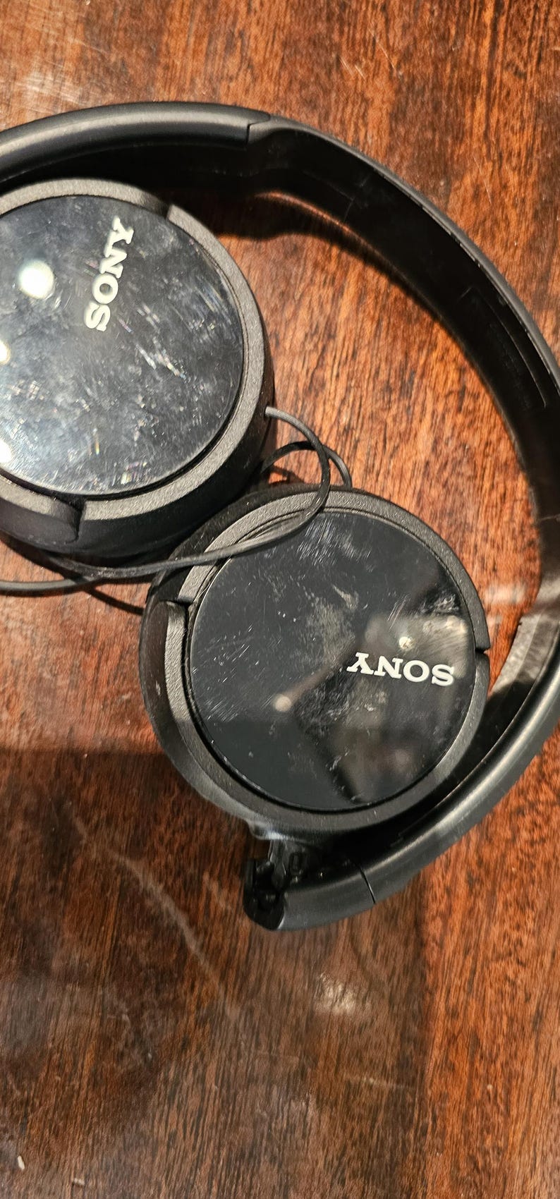 Op de afbeelding: Zwarte Sony over-ear hoofdtelefoon met een matzwarte hoofdband en ronde oorschelpen met een glanzende zwarte afwerking. Het Sony-logo is in het wit gedrukt in het midden van elke oorschelp. Dunne zwarte draden verbinden de twee oorschelpen.