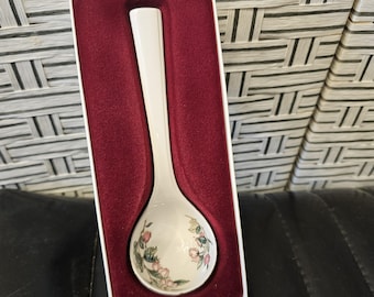 May include: A white ceramic spoon with a floral design in pink and green. The spoon is in a red velvet box.