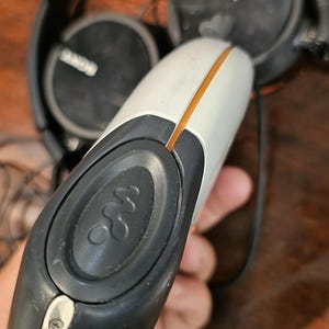 Op de afbeelding: Een witte en donkergrijze draagbare cassettespeler met het Walkman-logo op een ronde knop, geaccentueerd door een dunne oranje lijn. Het apparaat is gecombineerd met een zwarte Sony-hoofdtelefoon met ronde oorschelpen en een dunne hoofdband.