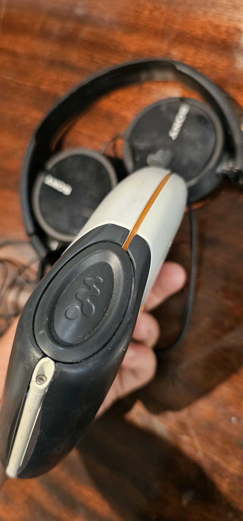 Op de afbeelding: Een witte en donkergrijze draagbare cassettespeler met het Walkman-logo op een ronde knop, geaccentueerd door een dunne oranje lijn. Het apparaat is gecombineerd met een zwarte Sony-hoofdtelefoon met ronde oorschelpen en een dunne hoofdband.