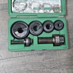 Puede incluir: Una caja de pl&aacute;stico verde abierta que contiene un juego de punzones y matrices de metal. La caja revela varias herramientas de corte circulares y una varilla roscada. El texto "GREENLEE UGOBUSER 35BB KNOCKOUT PUNCH KIT" es visible.