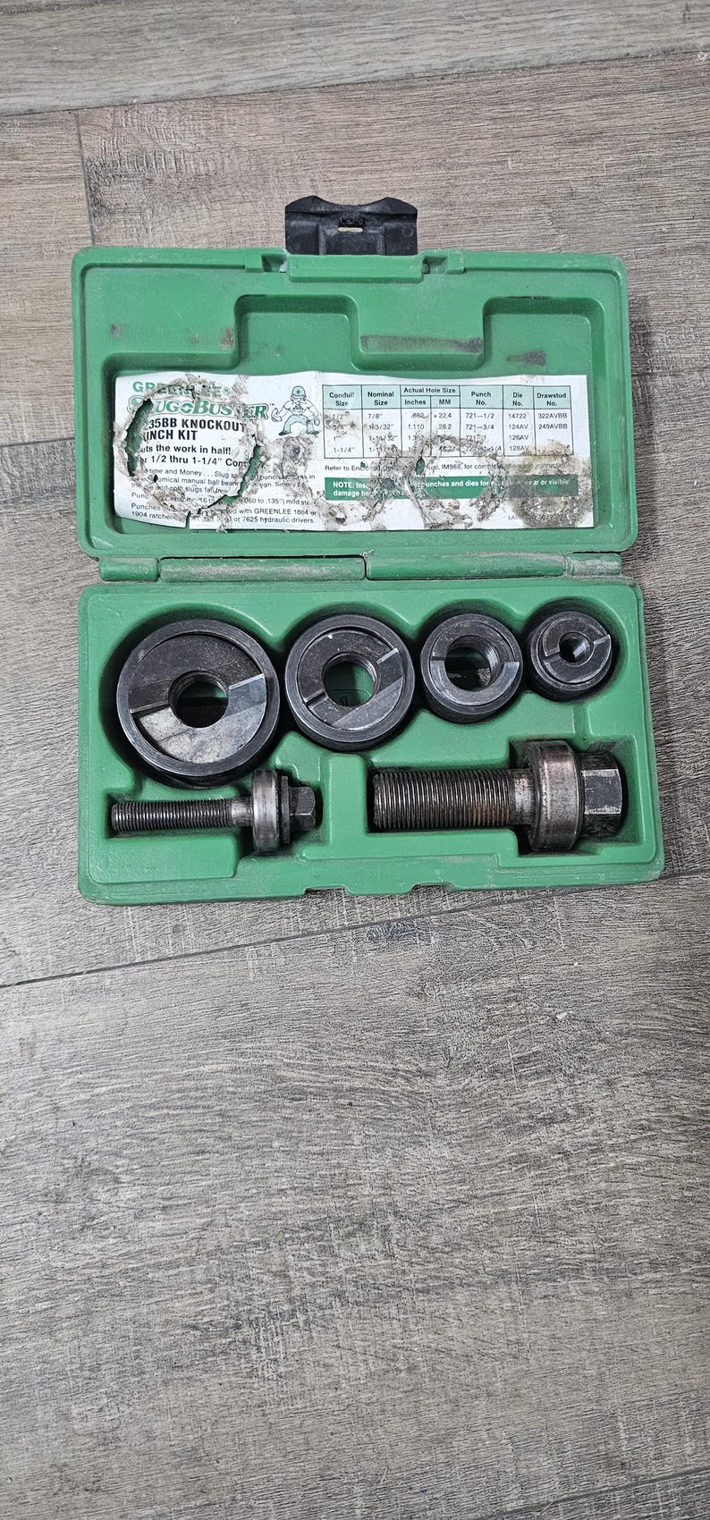 Puede incluir: Una caja de pl&aacute;stico verde abierta que contiene un juego de punzones y matrices de metal. La caja revela varias herramientas de corte circulares y una varilla roscada. El texto "GREENLEE UGOBUSER 35BB KNOCKOUT PUNCH KIT" es visible.