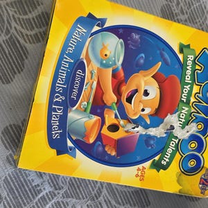 May include: A yellow square box for the Adikoo game, featuring a cartoon character painting a birdhouse. The text reads Adikoo, Reveal Your Natural Talents, and Discover Nature, Animals & Planets. The box indicates it is for ages 4-6.