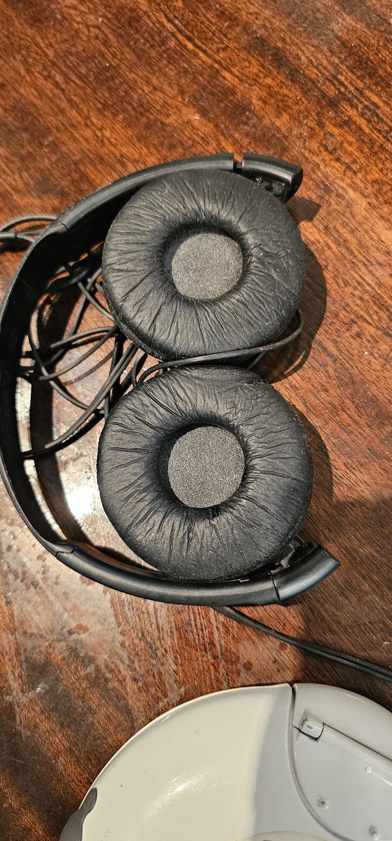 Op de afbeelding: Zwarte bedrade hoofdtelefoon met twee ronde, getextureerde oorkussens met een matte afwerking. De hoofdband is gemaakt van zwart plastic en bevat een dunne, ge&iuml;ntegreerde zwarte audiokabel die de twee oorschelpen met elkaar verbindt.
